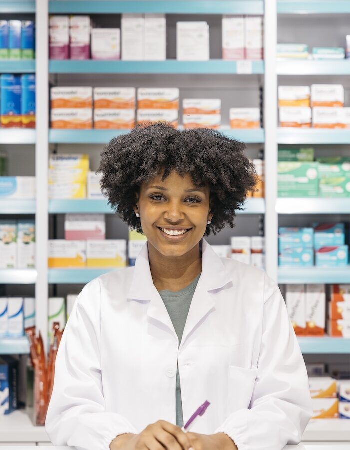Pharmacist smiling at pharmacy counter with medicine on shelves