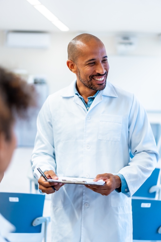 Smiling doctor holding clipboard talking with patient in hospital room