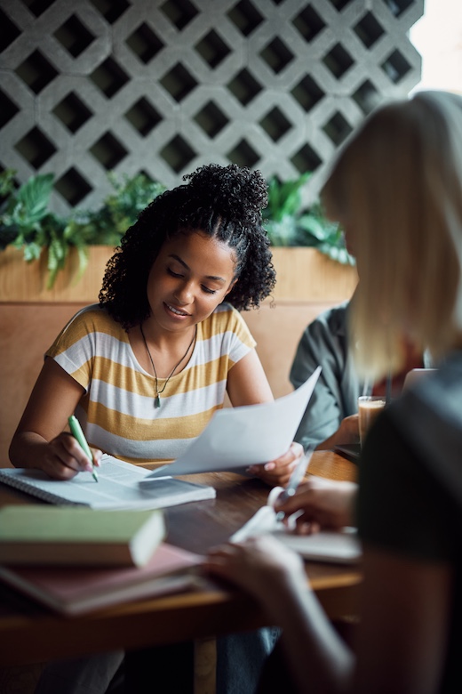 Young black woman taking notes while studying with friends in a cafe,